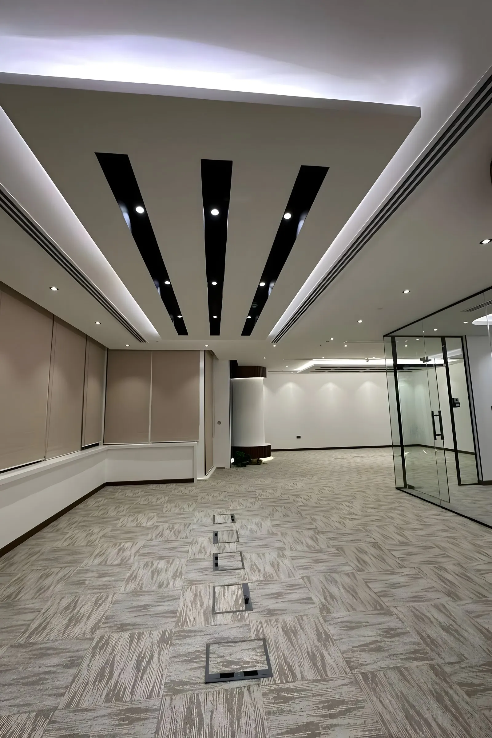 Large finished commercial interior with a slatted black-and-white ceiling, fabric wall panels and a glass door