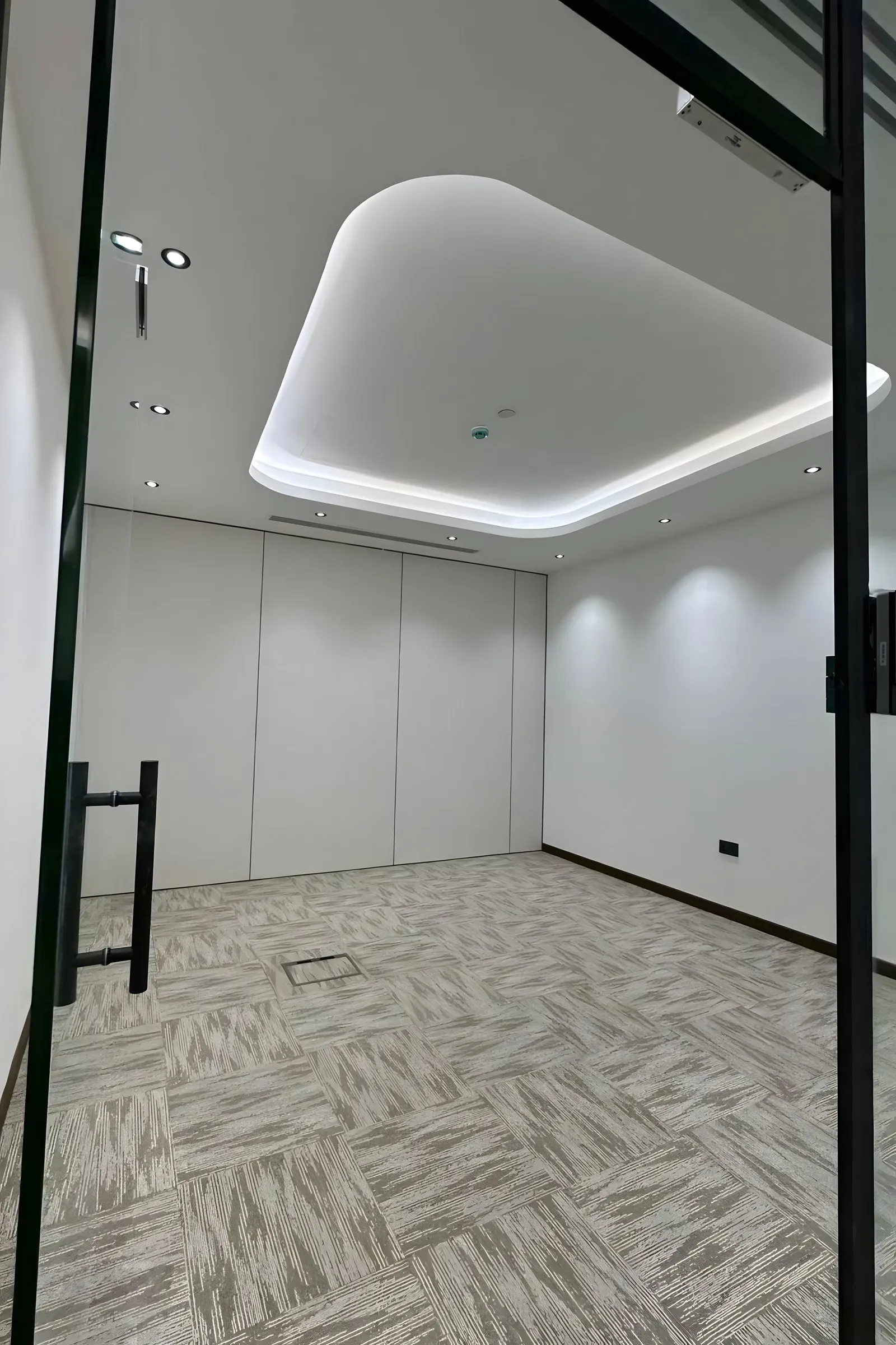 Finished commercial room with a recessed ceiling, white walls, fabric panels and a glass door