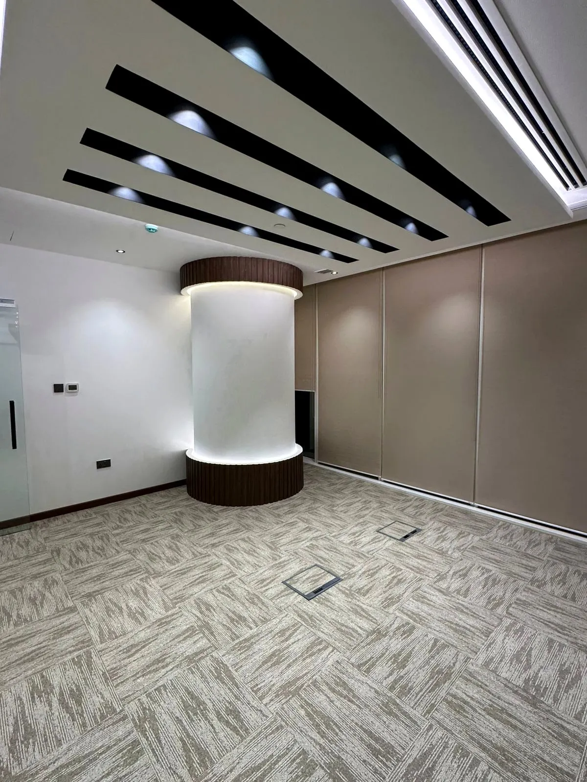 Finished office with a slatted ceiling, an LED-lit curved column and carpet tiles