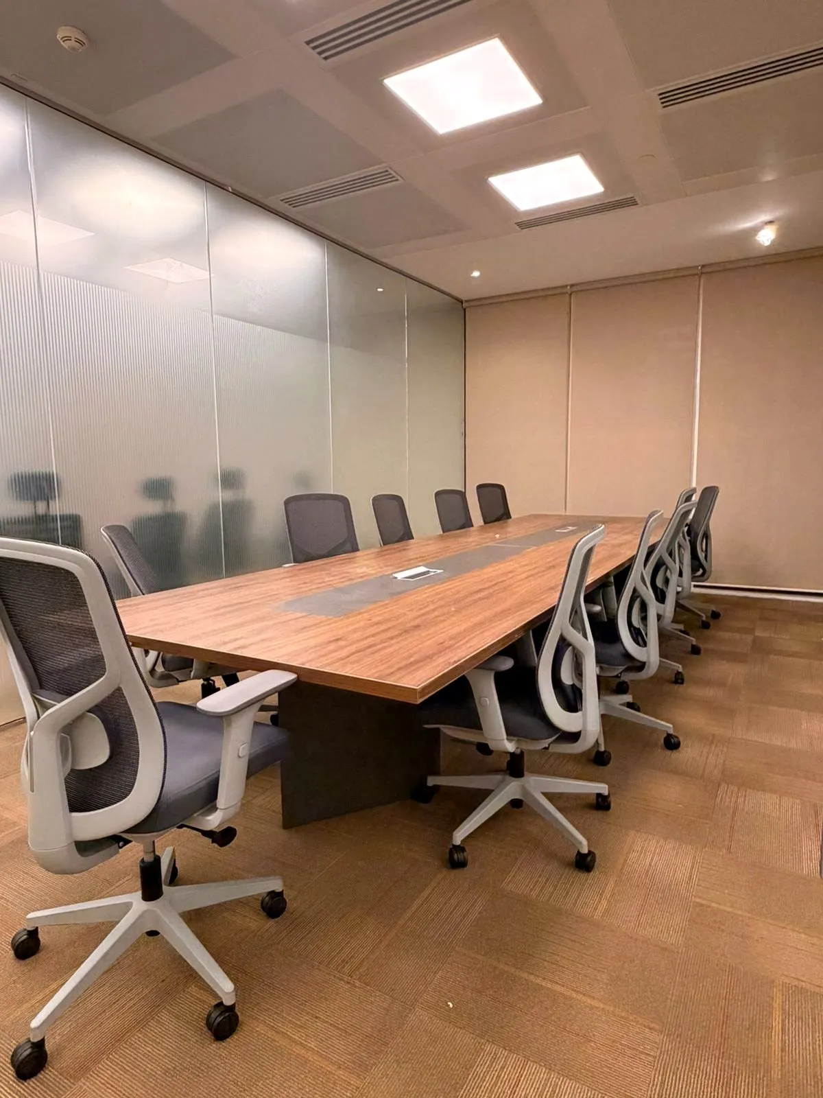 Finished meeting room with a long walnut-effect table, mesh chairs and a frosted glass partition