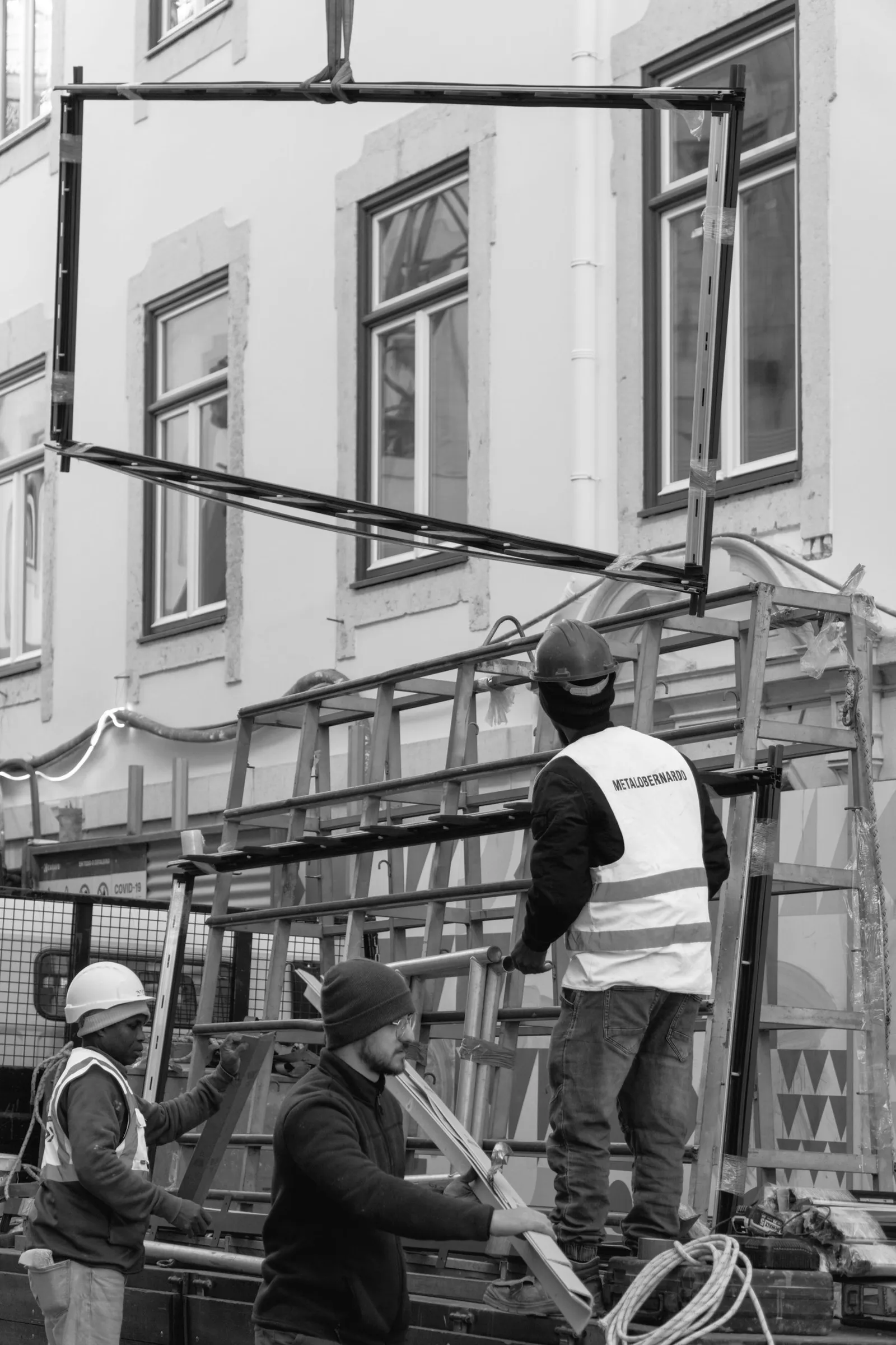 Worker in a hi-vis vest fitting an aluminium window frame at height beside scaffolding