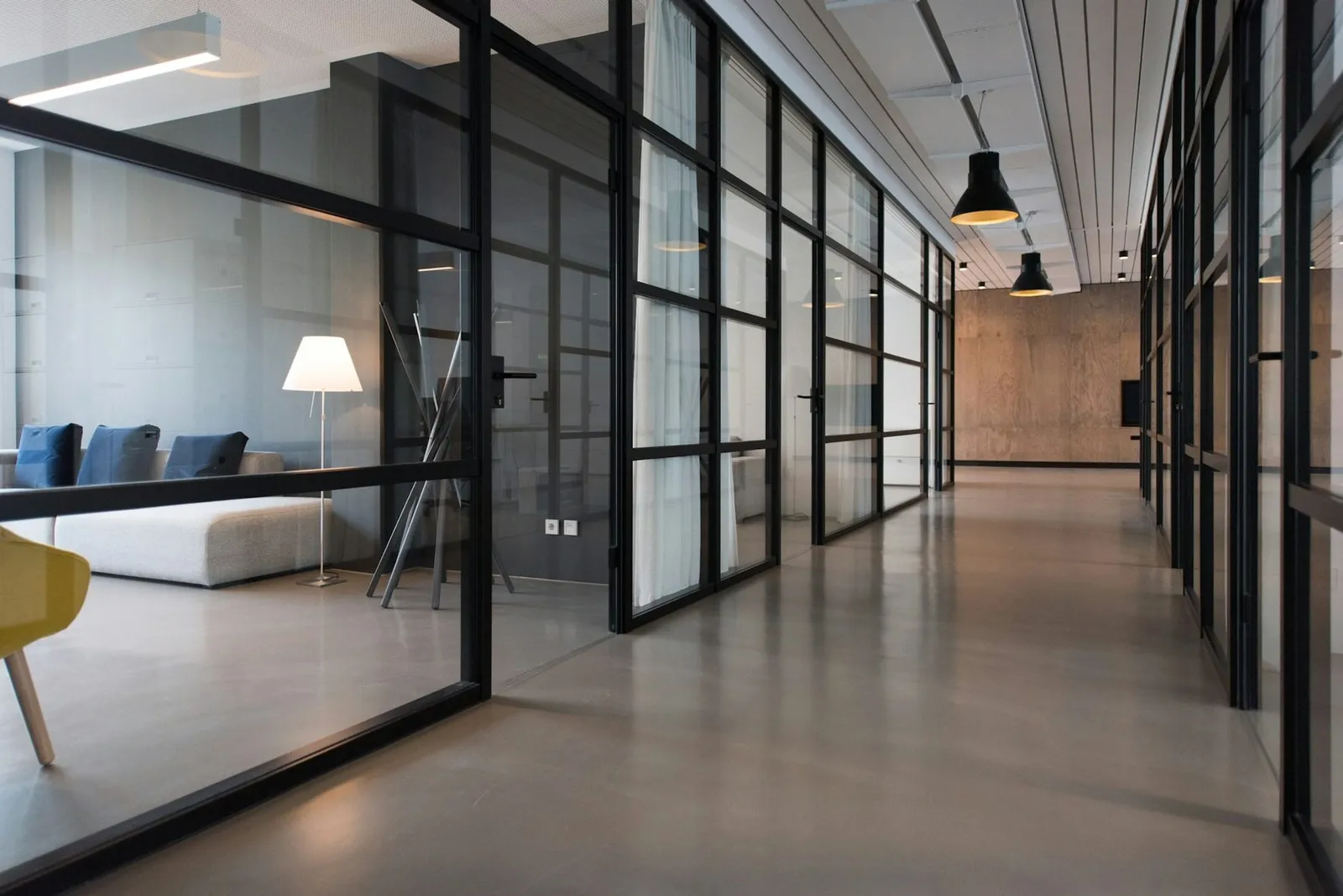 Finished office corridor with black-framed glass partitions and a polished floor